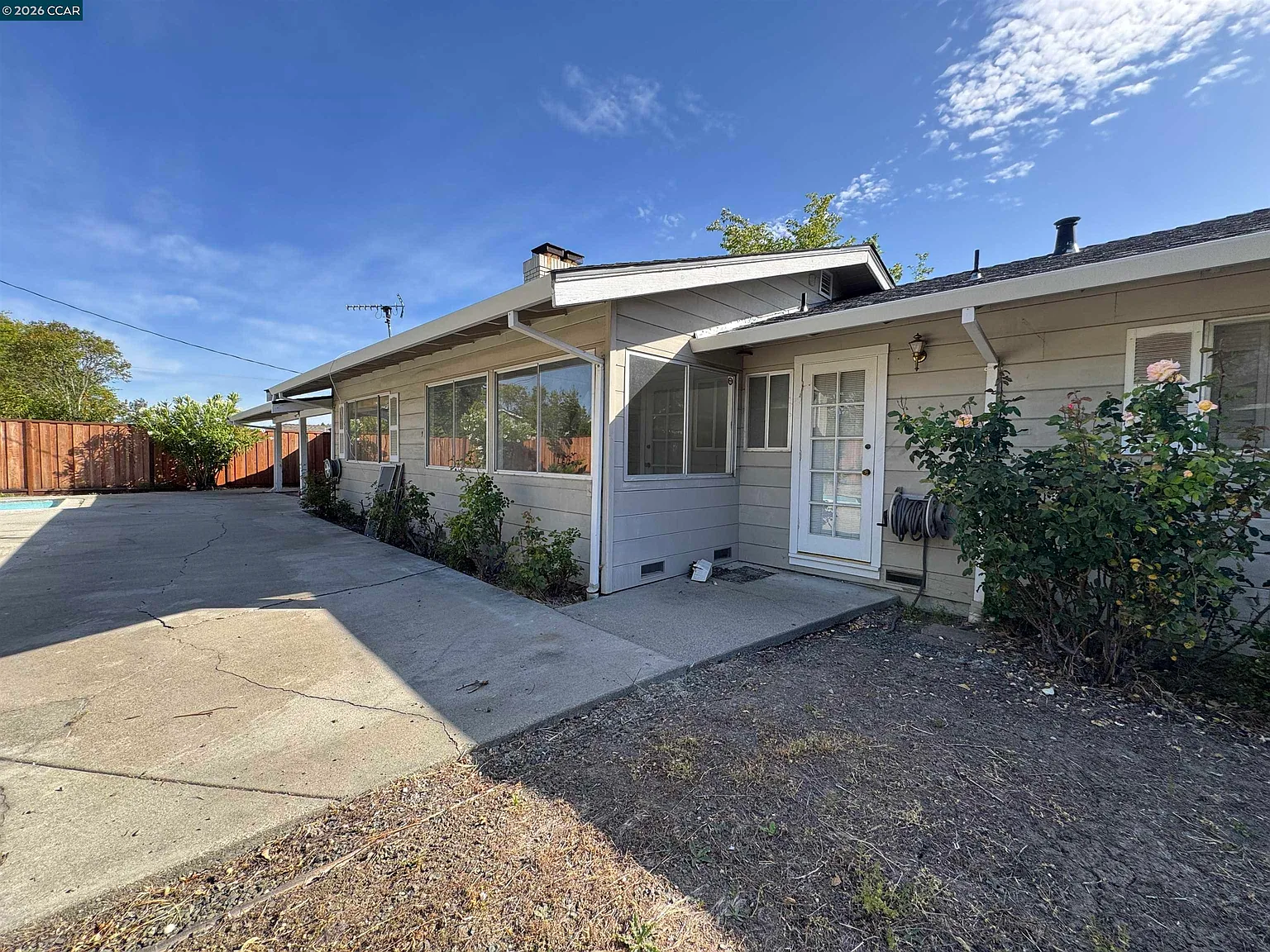 Rear elevation showing the deep concrete patio, sliding glass door access, and a single-story rear wing under California sun