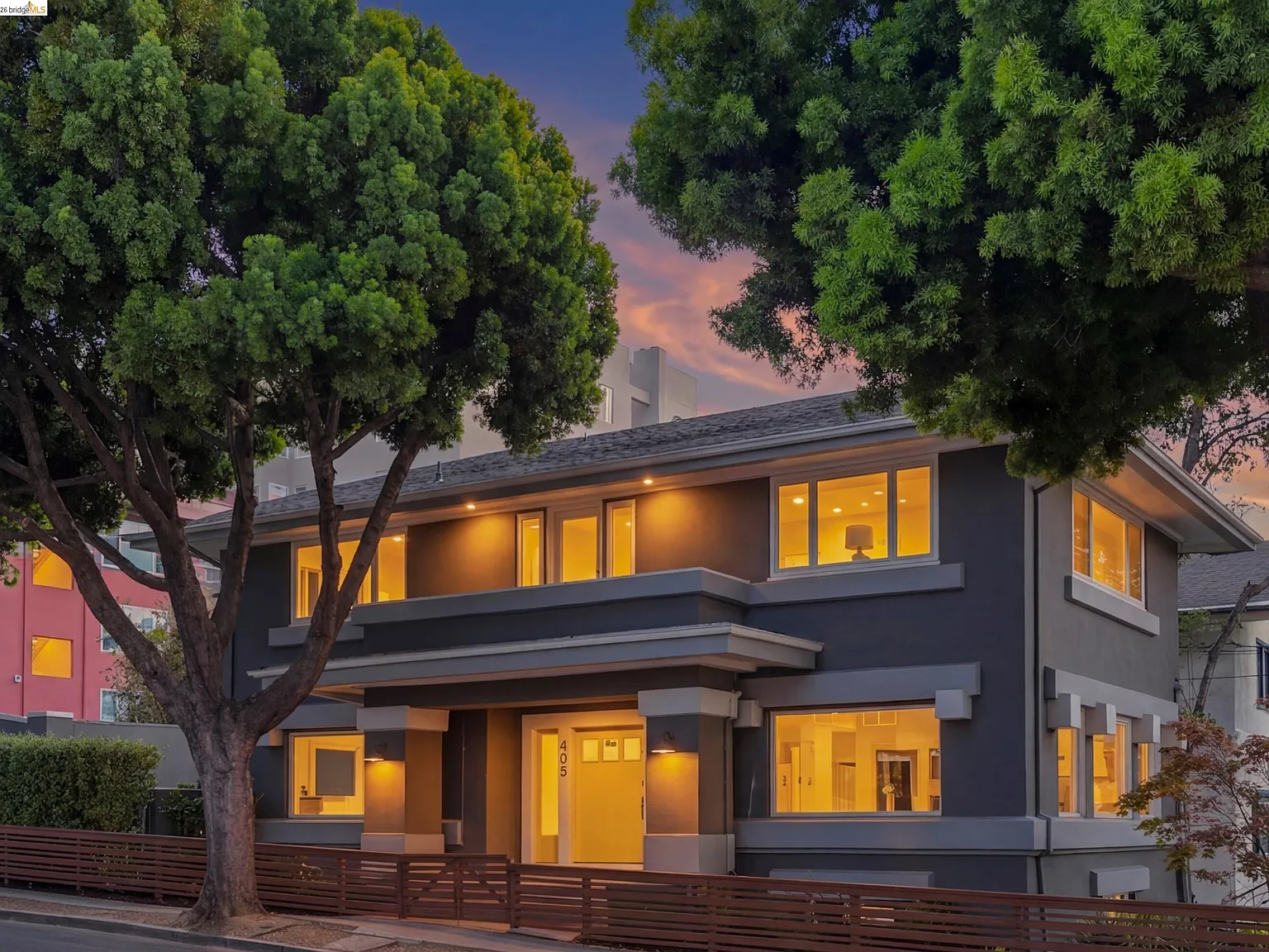 A two-story stucco home on Longridge Road photographed at twilight with warm interior light and a sunset sky behind the mature street trees