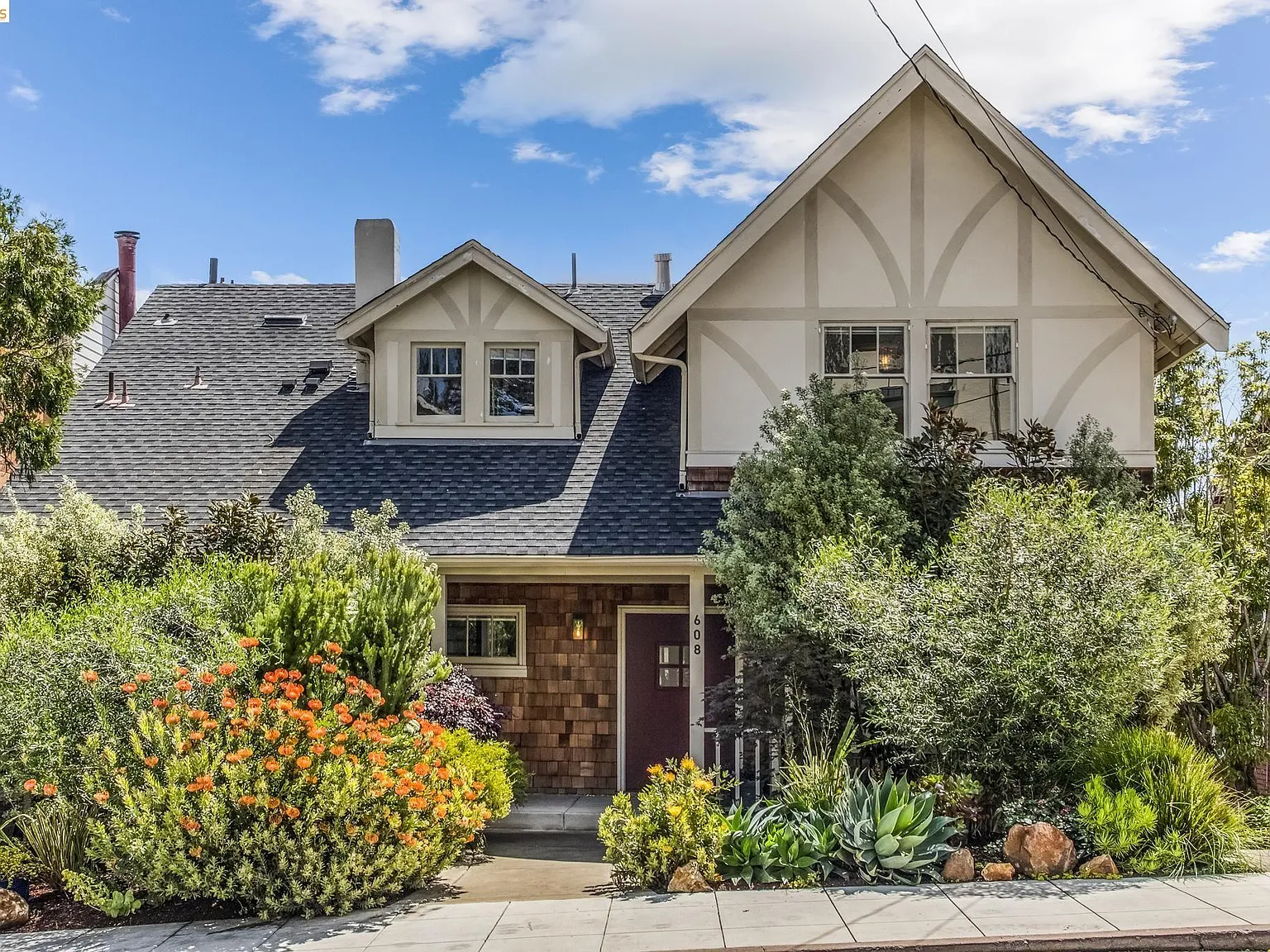 A storybook Tudor home on a Crocker Highlands street with steep gabled roof, decorative half-timbering, and bursts of orange flowers in the front garden