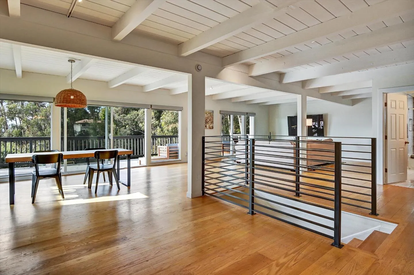 Vaulted great room at 635 Longridge with white-beamed ceiling, oak hardwood floors, dining area and railing detail opening to a sunlit rear patio